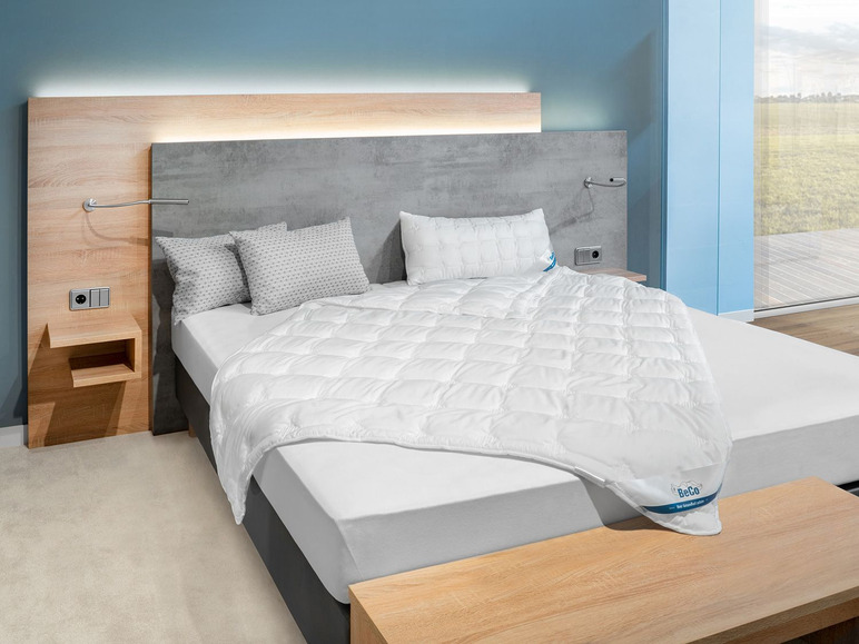 Une couette blanche Beco sur un lit avec une tête de lit en bois.