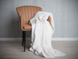 Une couverture blanche sur un fauteuil marron.