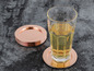 Un verre avec une boisson sur un dessous de verre en cuivre, à côté d'une pile de dessous de verre en cuivre.