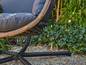 Une chaise grise en osier avec une base en métal noir dans le jardin.