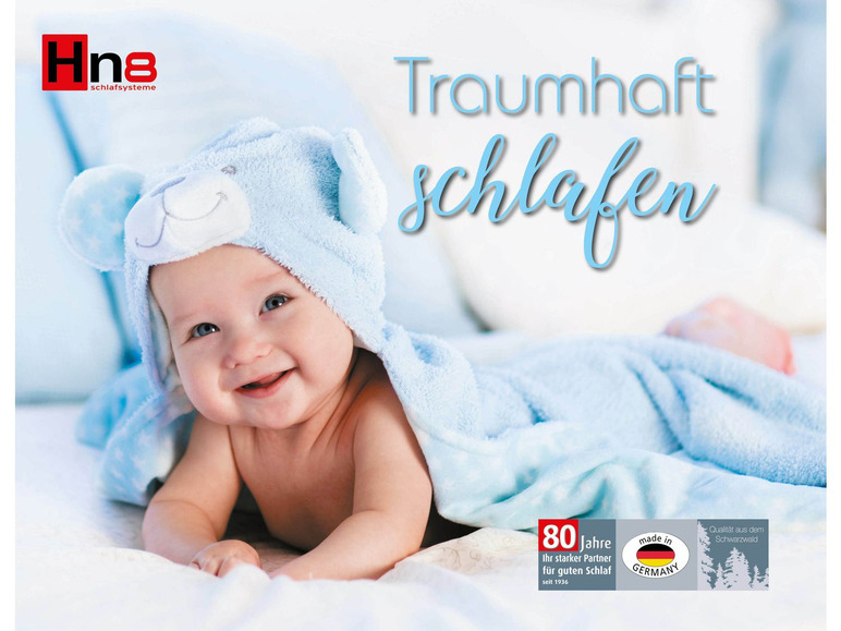 Un bébé dans une gigoteuse bleue avec le texte 'Traumhaft Schlafen' et la marque 'Hna Schlafsysteme'.