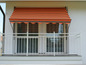 Un balcon blanc avec un store rayé orange.