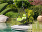 Un fauteuil suspendu avec des coussins verts, dans un jardin au bord de l'eau.
