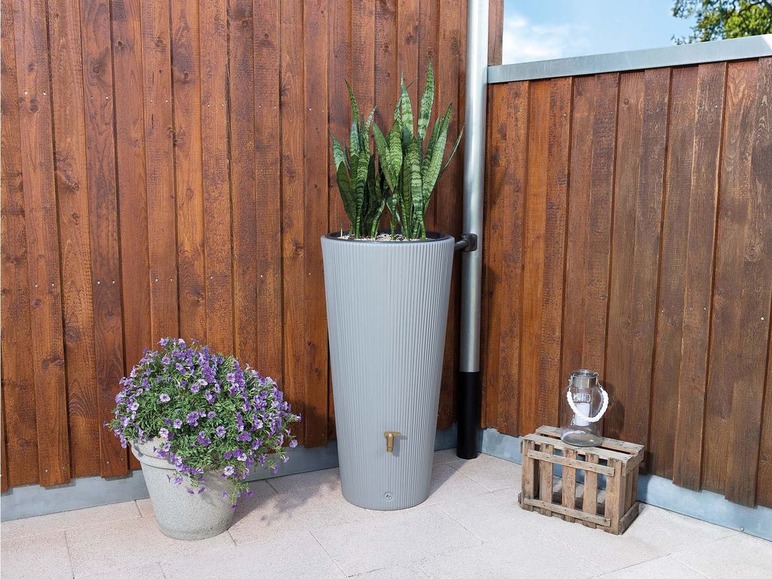 Un tonneau de pluie gris avec des plantes à côté d'une clôture en bois.