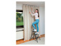 Une femme pose des rideaux avec un escabeau.