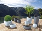 Un ensemble de pots ronds et ovales en gris et blanc, sur une terrasse en bois avec vue sur un lac et des montagnes.