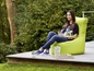 Une femme assise sur un pouf vert sur une terrasse.