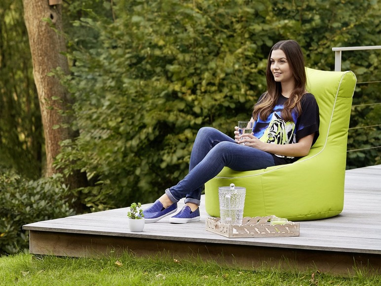 Une femme assise sur un pouf vert sur une terrasse.