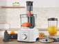 Un robot de cuisine Kenwood avec des carottes coupées, un blender avec du jus d'orange et divers accessoires.