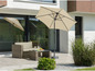 Un parasol beige avec un salon de jardin en osier sur une terrasse.
