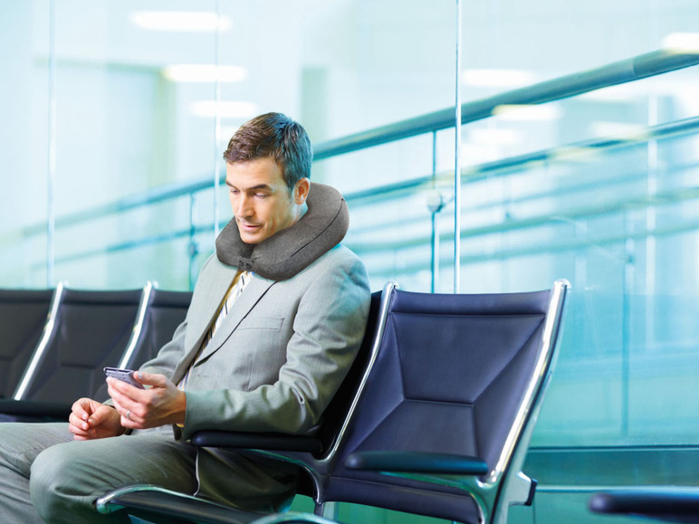 Un homme en costume gris avec un coussin de voyage dans une salle d'attente.