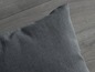 Une housse de coussin grise sur un sol en bois.