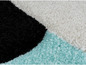 Détail d'un tapis doux blanc, noir et turquoise avec des motifs géométriques.