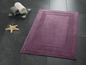 Un tapis de bain violet avec un bord décoratif.
