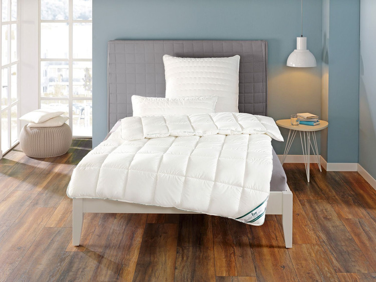 Une couette blanche sur un lit avec une tête de lit grise.
