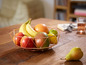 Un panier à fruits en cuivre avec des bananes, des pommes, de la mangue et des citrons.