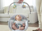 Un bébé assis dans un siège à bascule Fisher-Price avec un arc de jouets avec un lion et un éléphant.