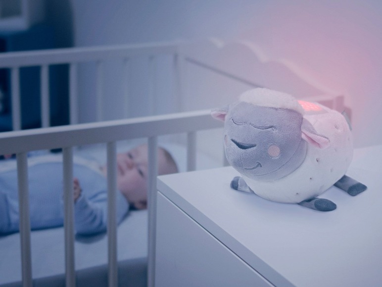Une veilleuse en forme de mouton à côté d'un bébé dans un berceau.