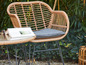 Une chaise en rotin avec un coussin gris et une table assortie dans un jardin.