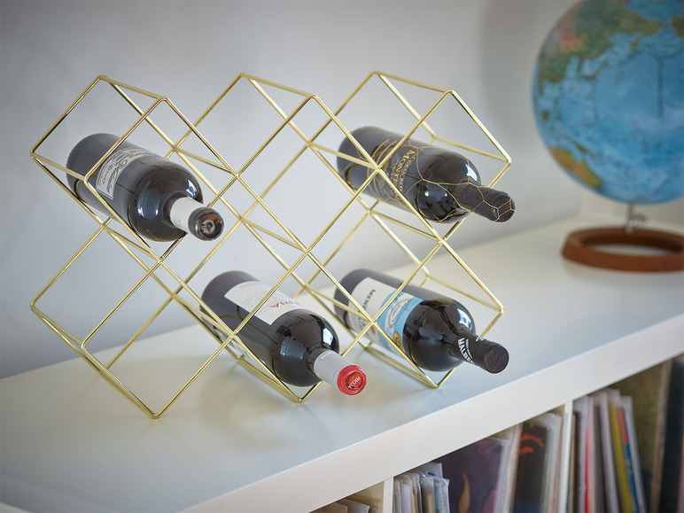 Un porte-bouteilles en or avec quatre bouteilles de vin sur une étagère blanche.