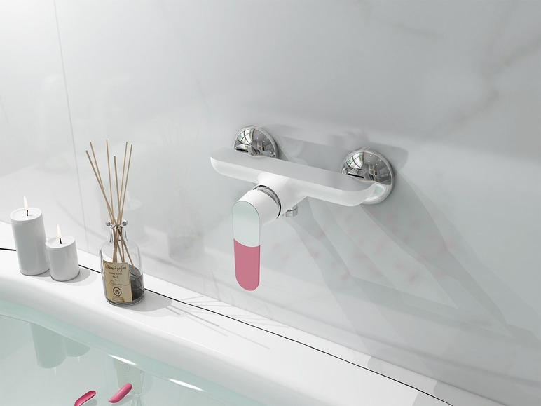 Un robinet de baignoire blanc avec des accents roses au-dessus d'une baignoire avec des bougies et un diffuseur.