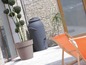 Un tonneau de pluie gris et un pot de terre cuite sur une terrasse avec deux chaises longues.