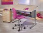 Un bureau en bois avec un fauteuil de bureau rose, une petite table de chevet blanche avec des tiroirs et un panier en fil de fer.