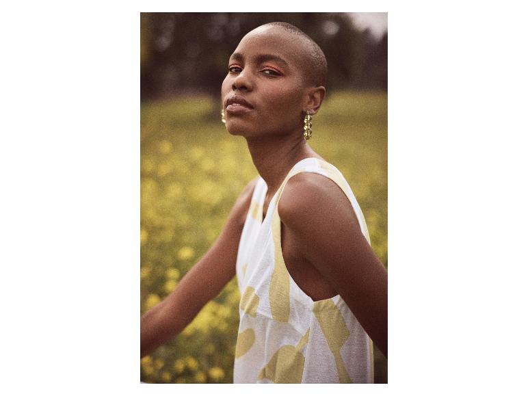 Modèle portant une robe sans manches à imprimé abstrait dans un champ de fleurs jaunes.