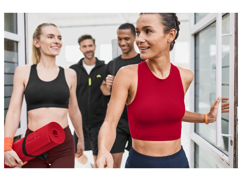 Des personnes en forme entrent dans un bâtiment, une femme porte un tapis de yoga rouge.
