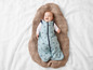 Un bébé dans un sac de couchage bleu avec un motif de voitures couché sur une couverture tricotée.