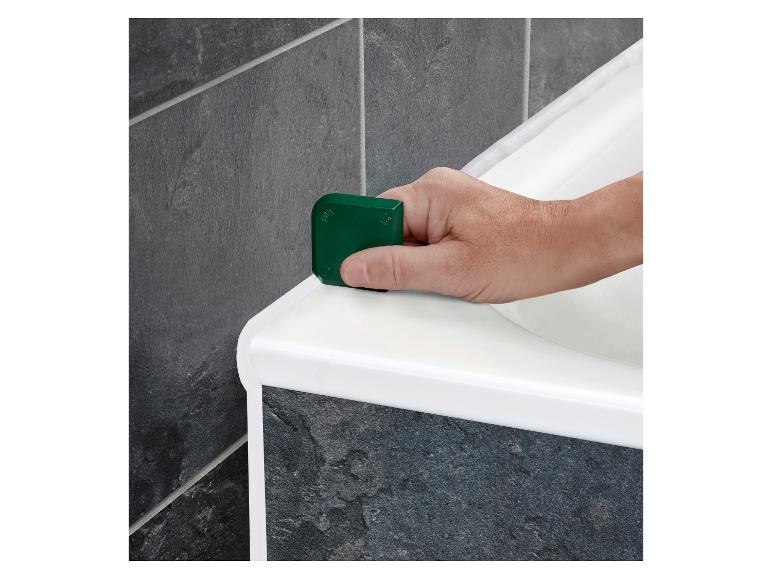 Main lissant le joint de silicone blanc le long d'une baignoire avec un outil vert.