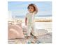 Bébé en vêtements crème près de coussins et jouets en bois, ambiance plage.