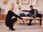Une femme en robe noire et en bottes à talons hauts pose dans un salon.