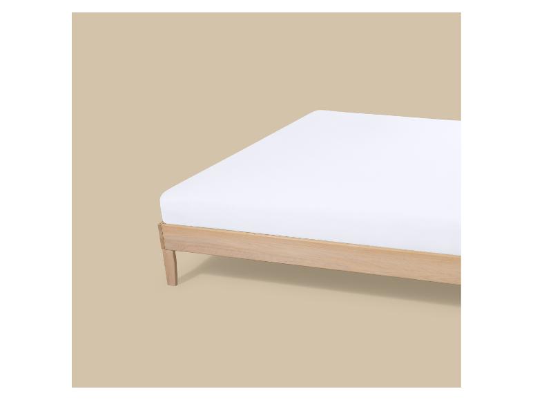 Matelas blanc sur un cadre de lit en bois clair sur fond beige.