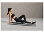 Une femme en vêtements de sport utilise un rouleau en mousse sur un tapis de yoga.