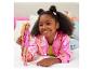 Une fille souriante joue avec une poupée Barbie sur un lit.