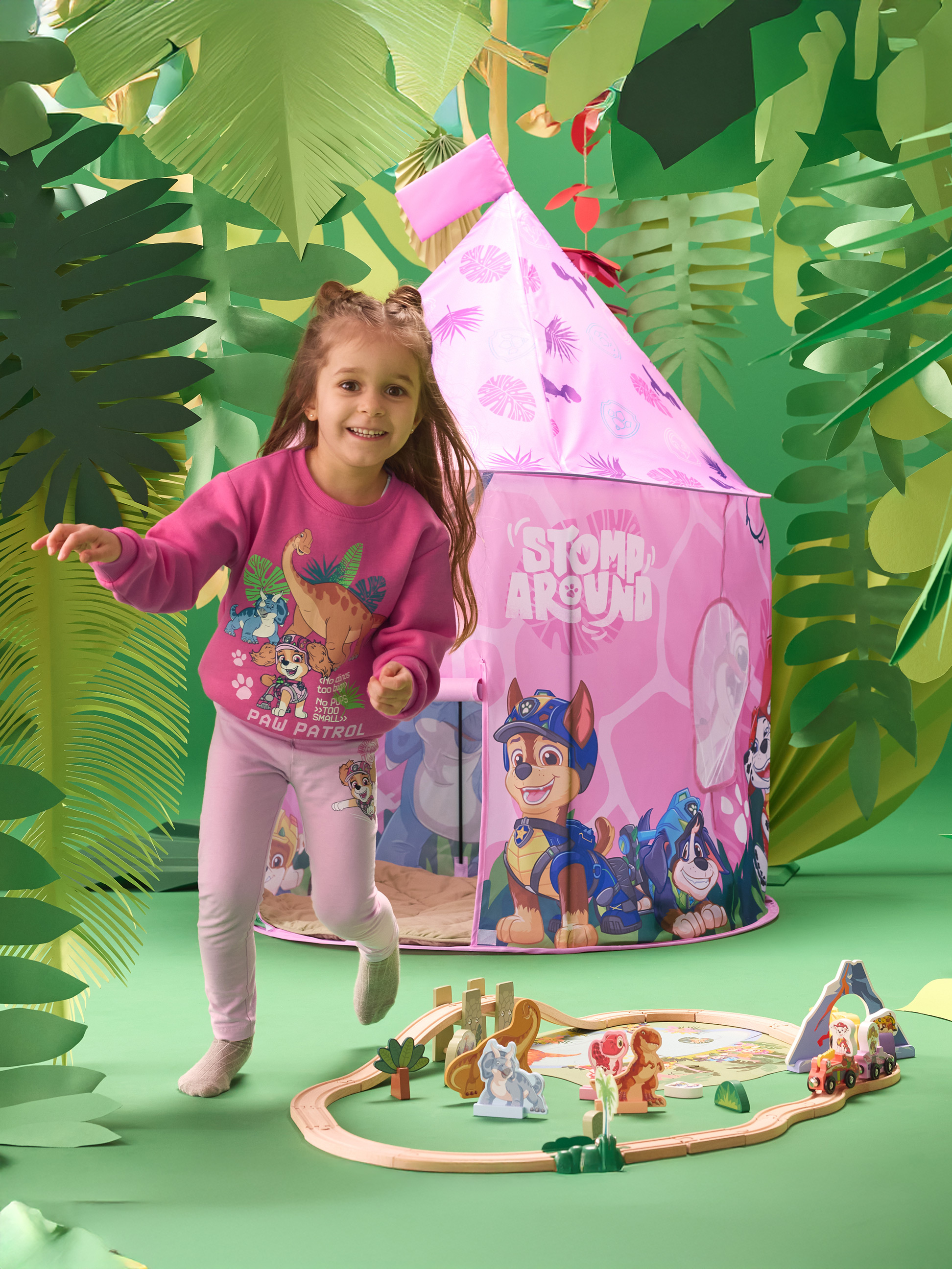Fille en sweat-shirt et legging roses, jouant avec une tente de jeu rose et un train en bois.