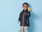 Un enfant portant un imperméable bleu et un pantalon gris tient un canard en caoutchouc jaune.