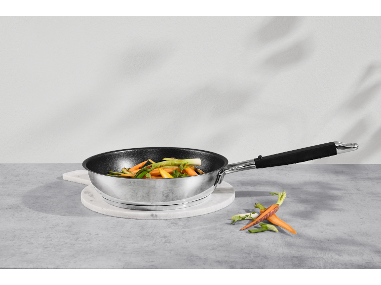Poêle avec légumes sur un dessous de plat en marbre, avec carottes et oignons verts à côté.