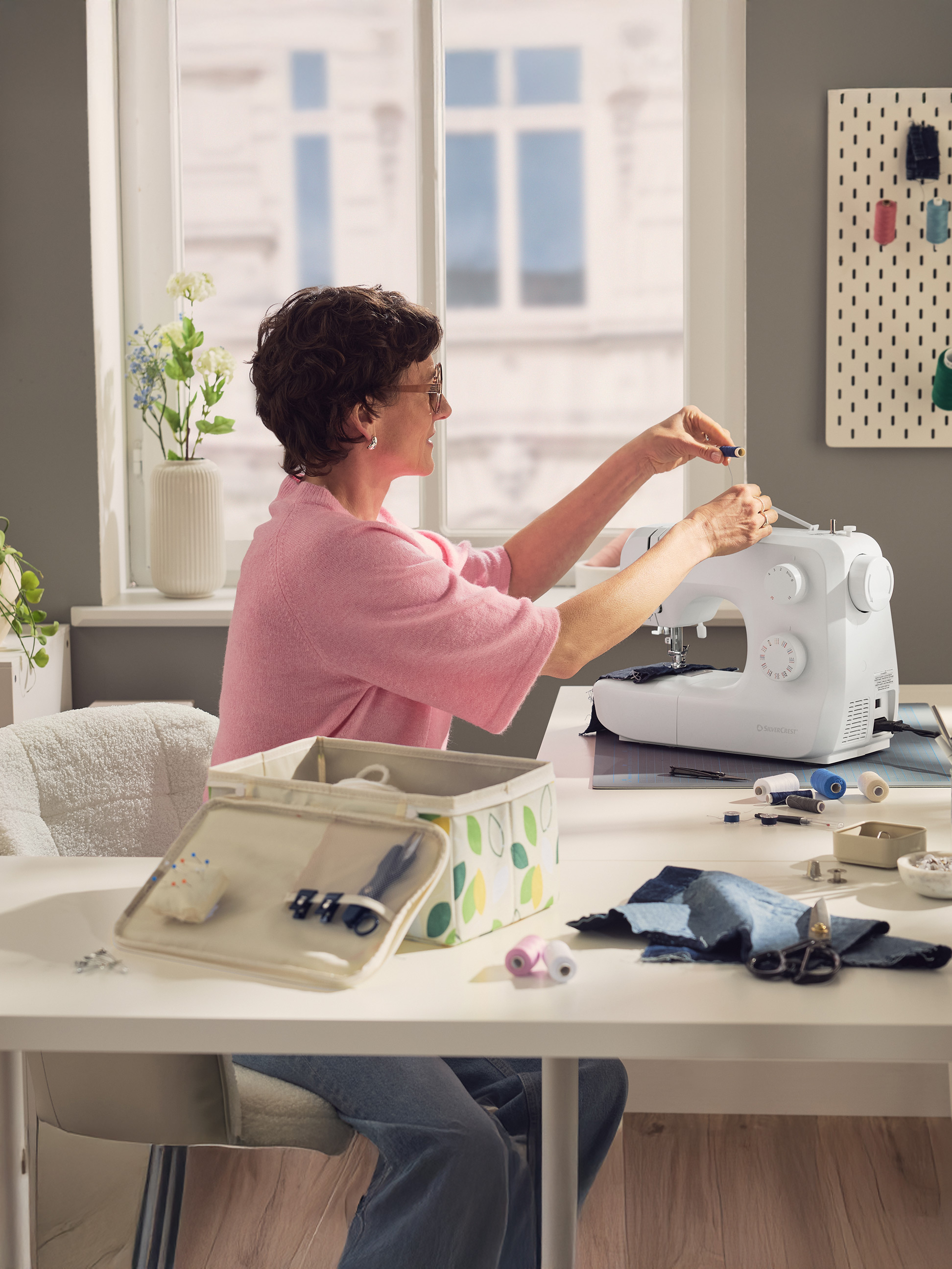 Femme cousant sur une machine à coudre, avec des accessoires de couture sur la table.