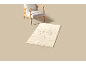 Fauteuil beige et tapis rectangulaire avec motif de rose sur fond clair.