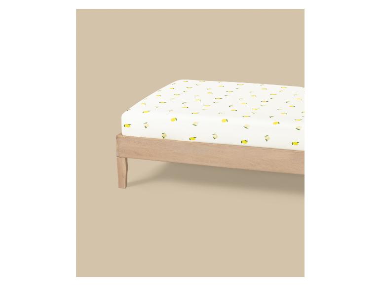 Drap-housse blanc à motif de citrons sur un cadre de lit en bois.