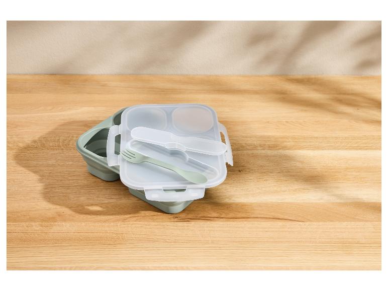 Boîte à lunch pliable verte avec couverts sur une table en bois.