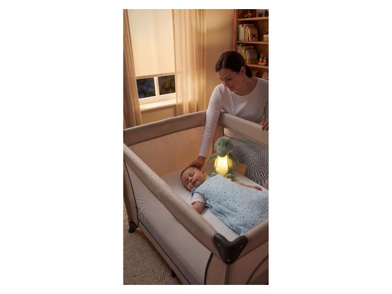 Mère couchant bébé dans un lit de voyage avec une peluche lumineuse.