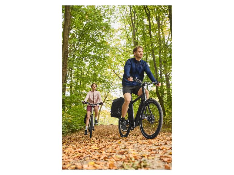 Deux personnes à vélo sur un chemin forestier couvert de feuilles d'automne.