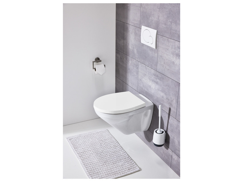 Une toilette blanche avec abattant intégré, une brosse de toilette et un tapis de bain.