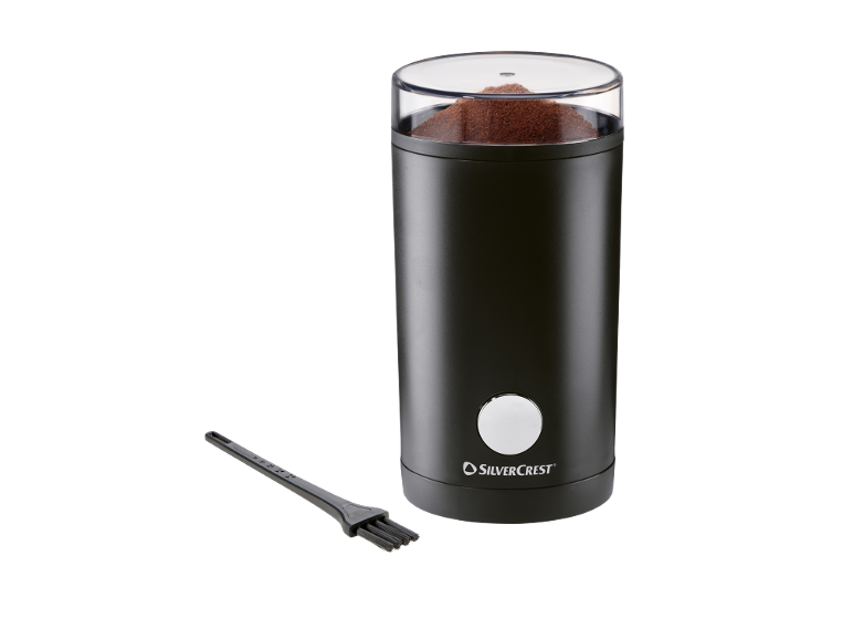Moulin à café électrique noir avec couvercle transparent rempli de café moulu et brosse de nettoyage.