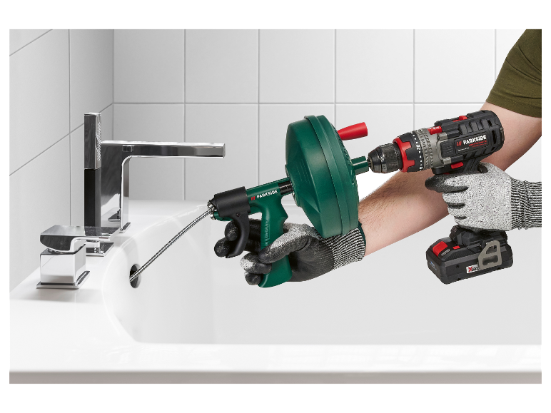 Une perceuse Parkside est utilisée pour actionner un nettoyeur de canalisation dans un lavabo de salle de bain.