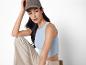 Femme portant un débardeur bleu clair et un pantalon beige, casquette grise.