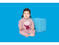 Bébé en pyjama rose avec ourson et écharpe, assis à côté d'un cube bleu.